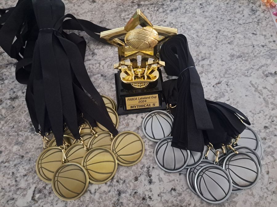 Gold and silver basketball medals on black ribbons around a gold star trophy with an engraved plate