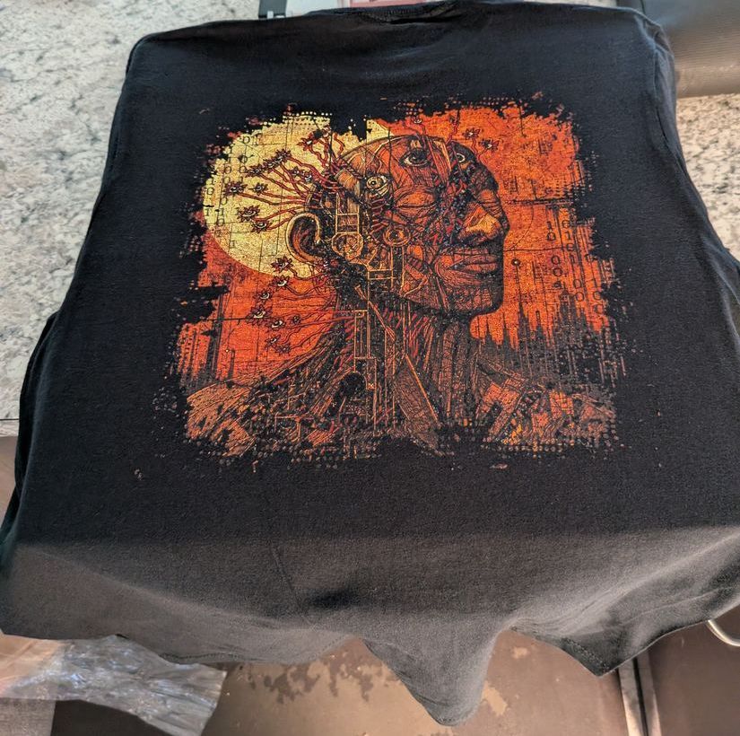 The back of a black t-shirt with a full-colour illustrated print, laid flat on a heat press