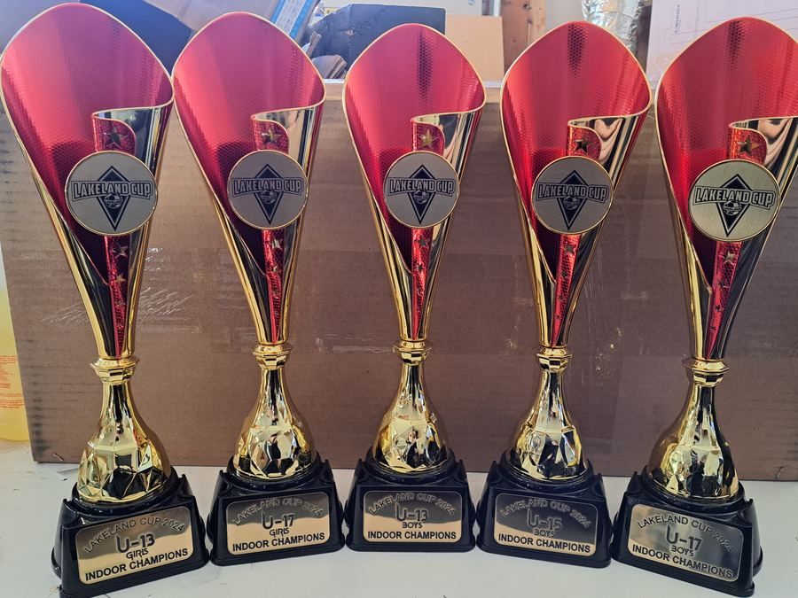 Five red and gold cup trophies with engraved plates, lined up on a table